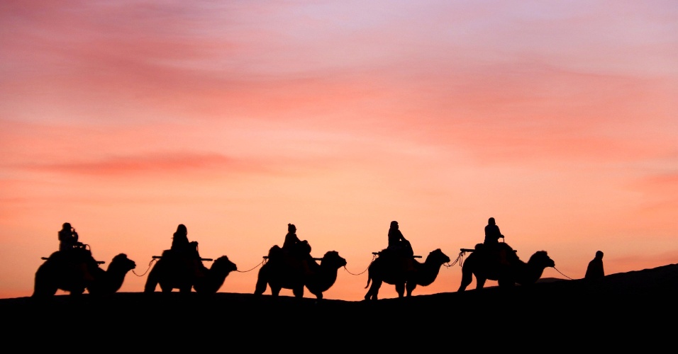 08.out.2105 - Turistas montam em camelos durante passeio pela colina Mingsha, na província de Gansu, na China