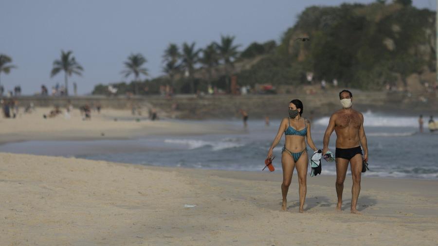 Casal com máscara de proteção caminha na praia do Arpoador, no Rio de Janeiro - 