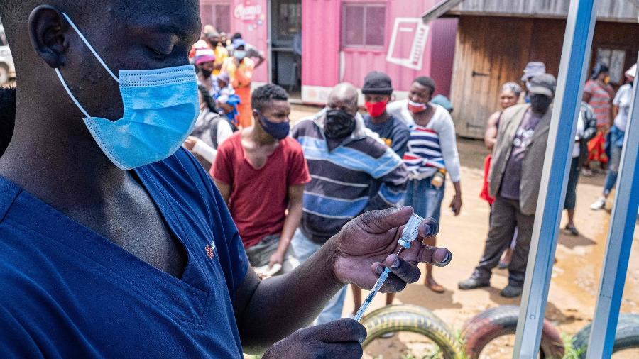 Profissional de saúde enche seringa com dose de vacina contra covid-19 enquanto as pessoas fazem fila em um assentamento na África do Sul - EMMANUEL CROSET / AFP