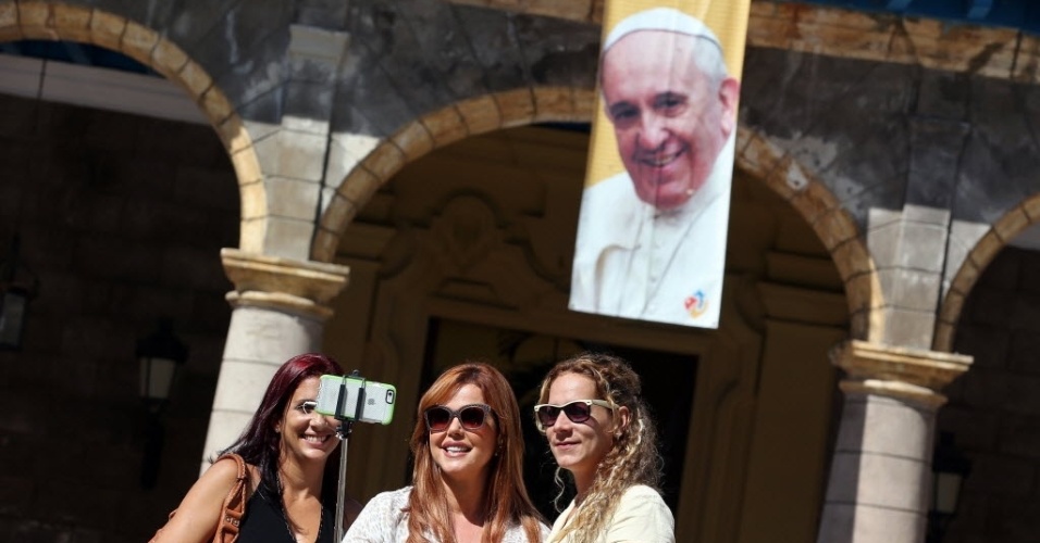 18.set.2015 - Três turistas tiram "selfie" perto de um pôster com a imagem do papa Francisco, em Havana, Cuba. O papa Francisco começará no próximo sábado (19) sua 10ª viagem internacional, um périplo que o levará a Cuba e aos Estados Unidos durante nove dias, nos quais fará 26 discursos
