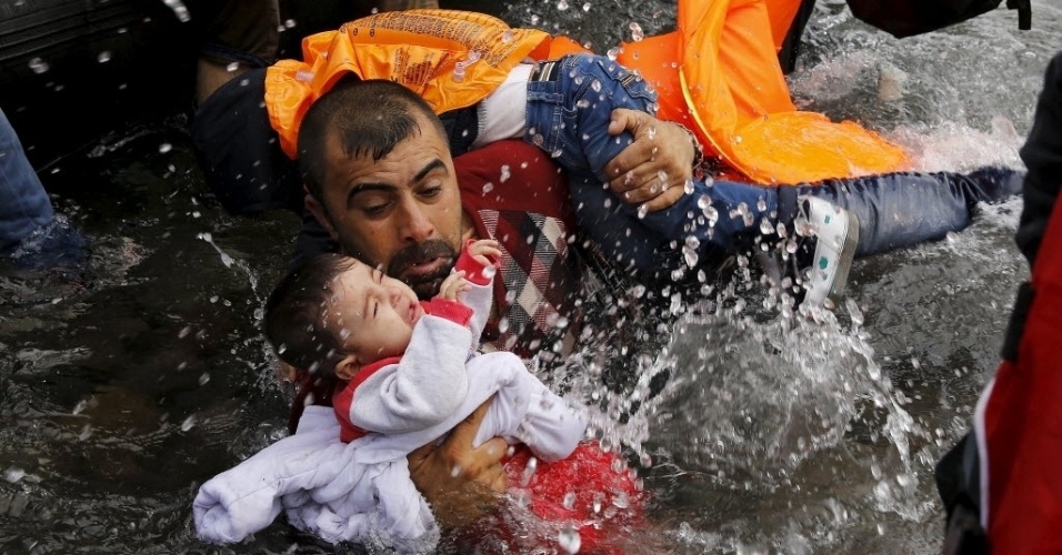 24.set.2015 - Refugiado sírio segura criança enquanto se esforça para sair de um bote na ilha grega de Lesbos. A chegada à Grécia acontece depois dele e outros refugiados atravessarem parte do mar Egeu, na Turquia