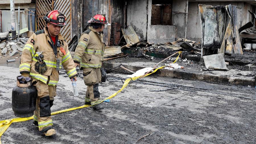 23.jan.2020 - Bombeiros caminham em frente a casas destruídas pela explosão de caminhão-tanque em Lima - AFP