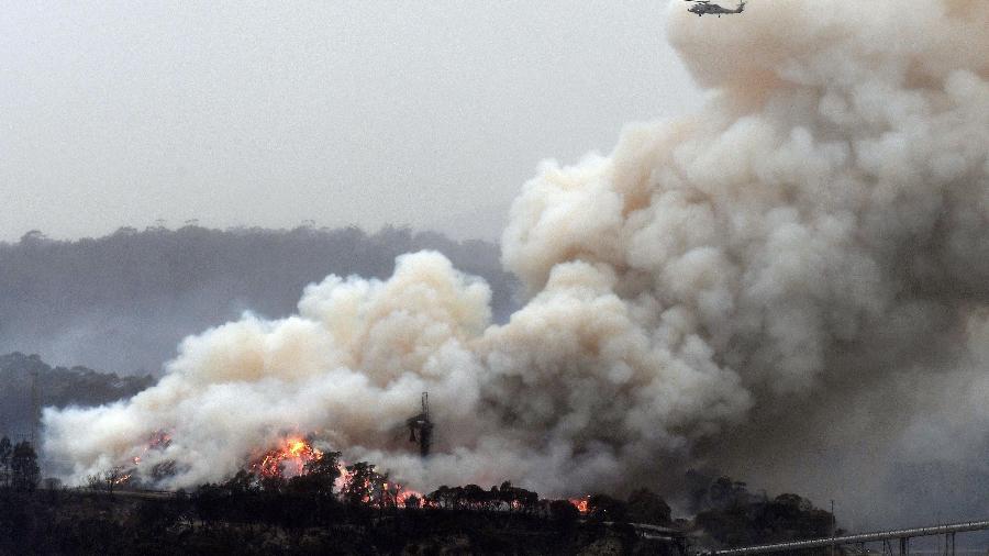 6.jan.2020 - Helicóptero militar sobrevoa incêndio florestal em Eden, Nova Gales do Sul, Austrália - Saeed Khan/AFP