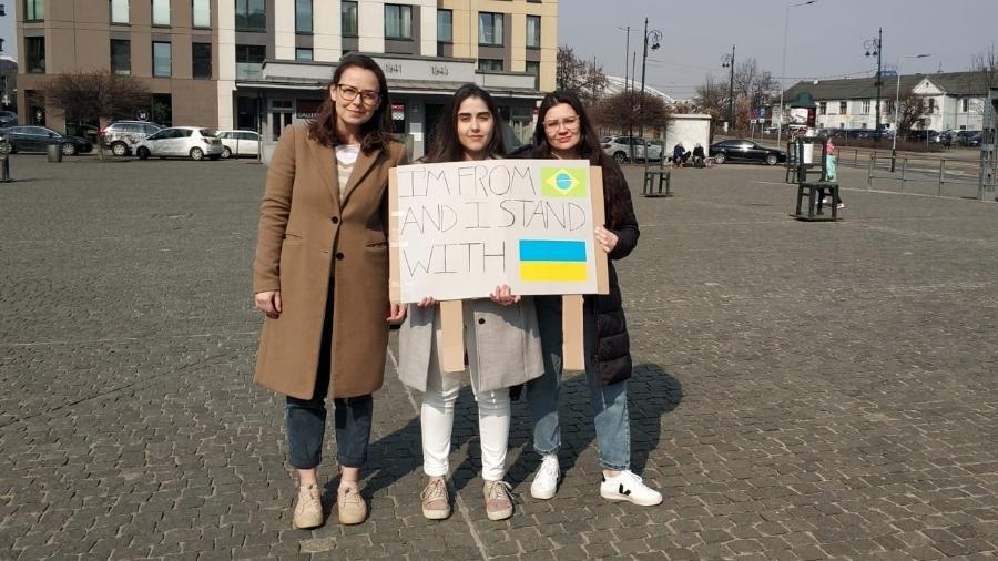As brasileiras Letícia Friolle, Lara Guedes e Marciele Silva (da esq. para a dir.) seguram cartaz de apoio aos refugiados ucranianos em Cracóvia, na Polônia. O texto diz em inglês: "Sou do Brasil e estou com a Ucrânia" - Arquivo pessoal