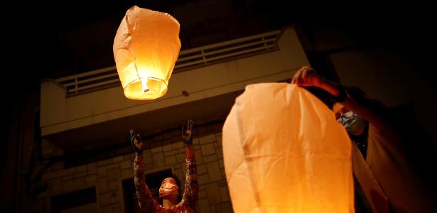 Pessoas usam máscaras enquanto acendem lanternas de papel em memória daqueles que morreram devido ao surto da covid-19 em San Giorgio, Itália