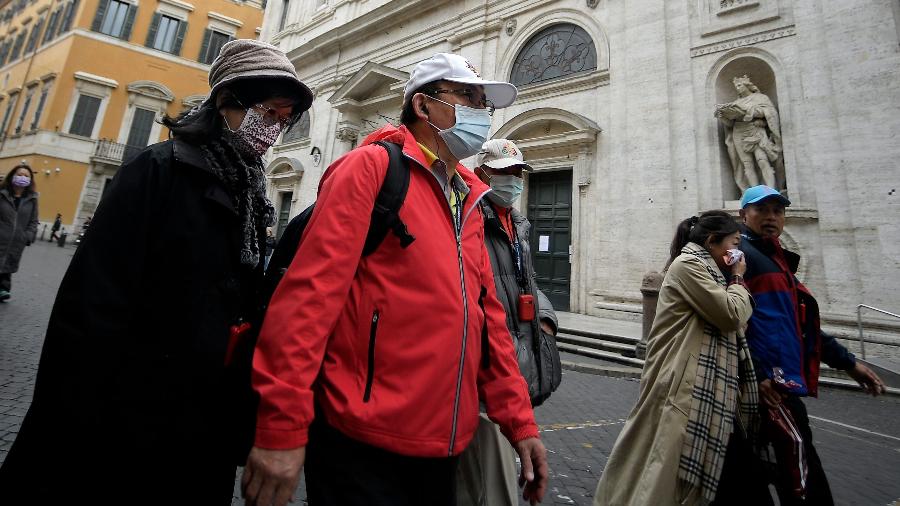 Usando máscaras, turistas asiáticos passam em frente à Igreja San Luigi dei Francesi, em Roma, fechada por conta do coronavírus - Filippo Monteforte/AFP
