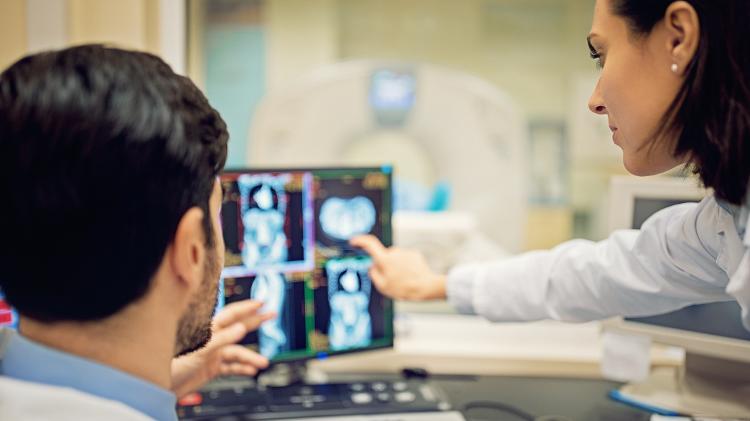 Médicos analisando exame de ressonância magnética em tela de computador Médicos analisando exame de ressonância magnética em tela de computador