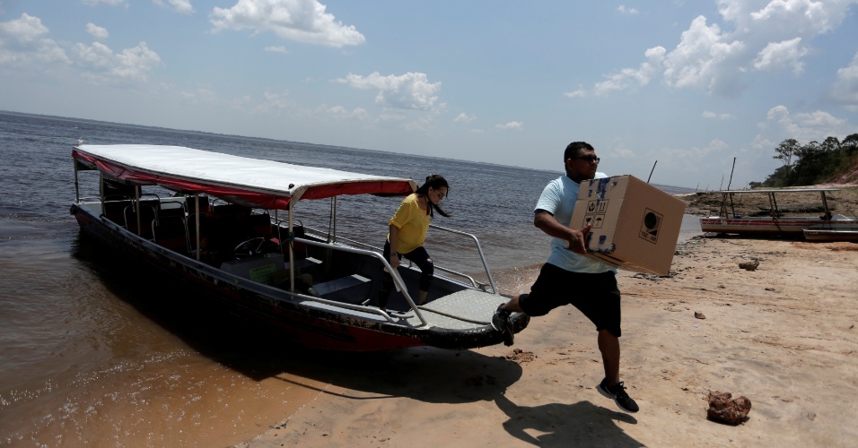 Funcionários carregam urnas em caixas no assentamento Nazaré, à margem do rio Amazonas