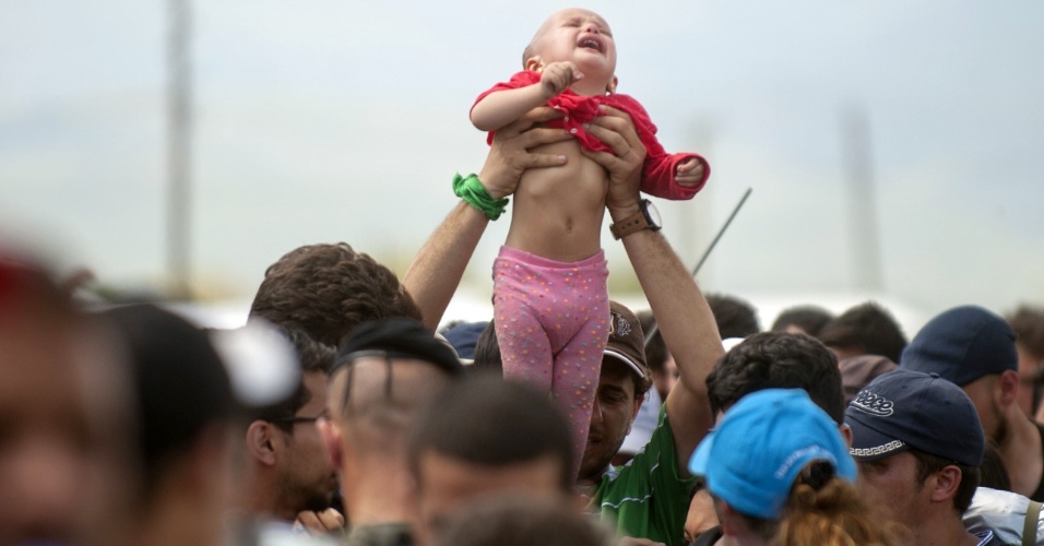 14.set.2015 - Homem suspende uma criança acima da multidão de imigrantes e refugiados que esperam para embarcar em um trem depois de cruzar a fronteira entre a Macedônia e a Grécia 
