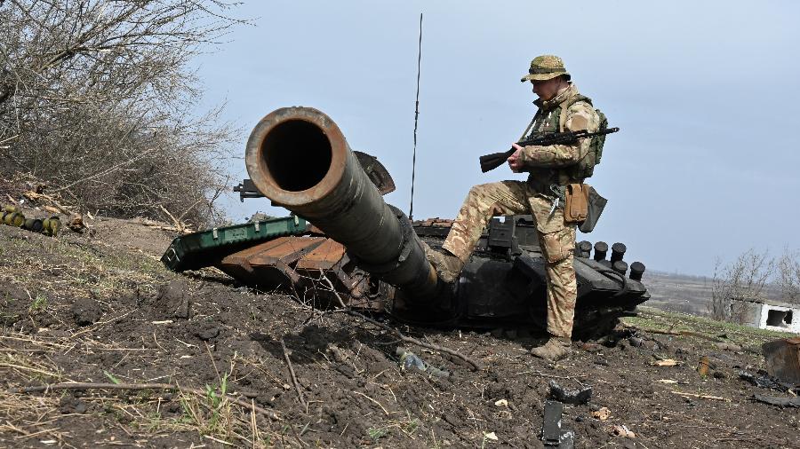 01.abr.2022 - Um soldado ucraniano verifica os destroços de um tanque russo queimado fora da vila de Mala Rogan, a leste de Kharkiv. - SERGEY BOBOK / AFP