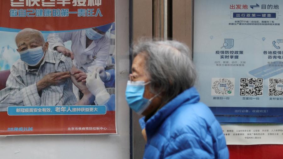 Pessoa passa por cartaz encorajando os mais velhos a tomarem a vacina contra a covid-19 - Tingshu Wang/REUTERS