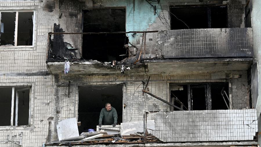 Um morador de um prédio residencial danificado observa enquanto limpa os escombros após o ataque russo em Kiev hoje - Sergei SUPINSKY / AFP