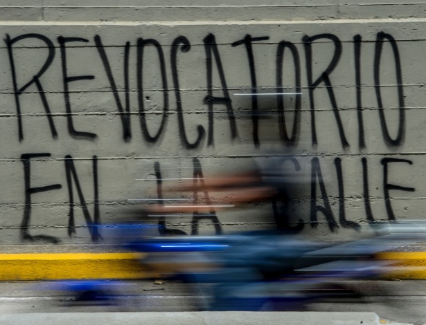 Homem passa de moto por pichação que diz "(o referendo) revogatório nas ruas", em Caracas, na Venezuela - Federico Parra/AFP