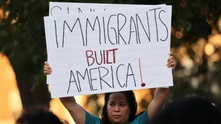 A woman on the night watch holds a banner that reads 'Immigrants Built America' - Getty Images - Getty Images