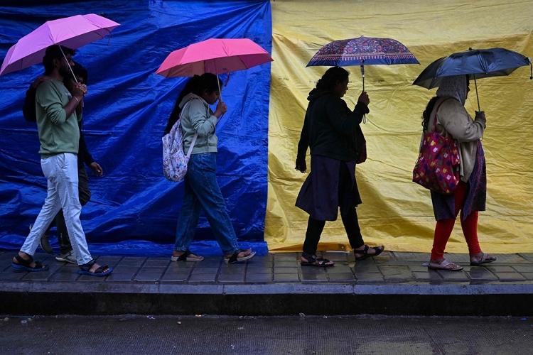 Mulheres caminham com sombrinhas em ruas de Bangalore; chuva ficou intensa no local durante ciclone Fengal