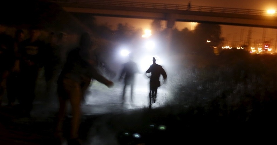 5.ago.2015 - Imigrantes são iluminados por lanternas usadas por policiais enquanto correm para atravessar uma cerca, durante tentativa de atravessar o Canal da Mancha, em Frethun, próximo a Calais, na França