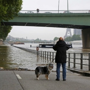 Homem anda com cachorro e tira foto em frente ao rio Sena, em Paris, que transbordou após dias de chuva