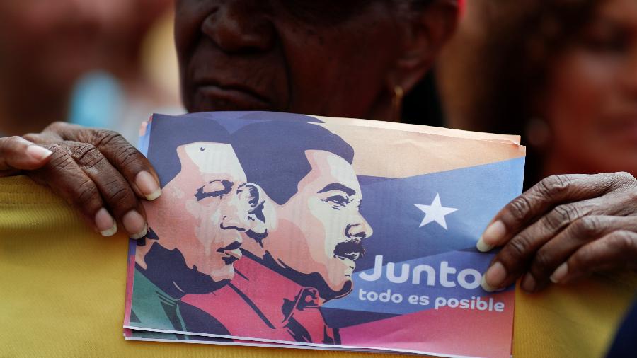 Eleitora de Nicolás Maduro segura cartaz com a imagem do presidente e de Hugo Chávez