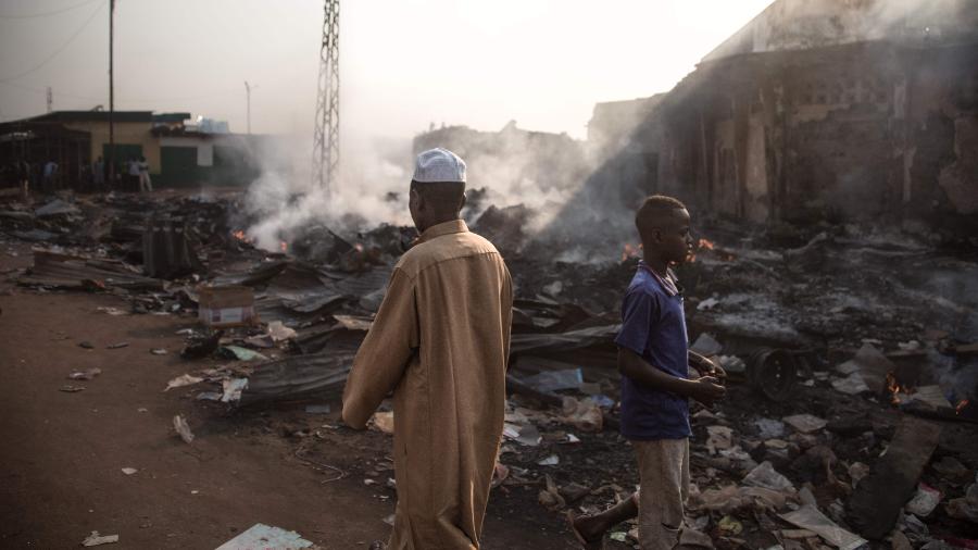 26.dez.2019 - Duas pessoas caminham nos destroços deixados após um confronto em Bangui, na República Centro-Africana - Florent Vergnes/AFP