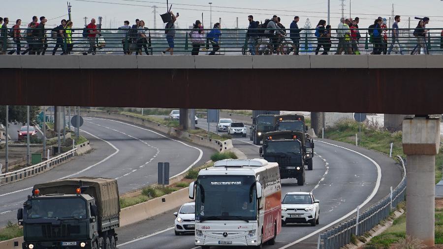 Veículos militares passam por baixo de uma ponte que é atravessada por voluntários a caminho do bairro La Torre para ajudar nos trabalhos de limpeza, em Valência