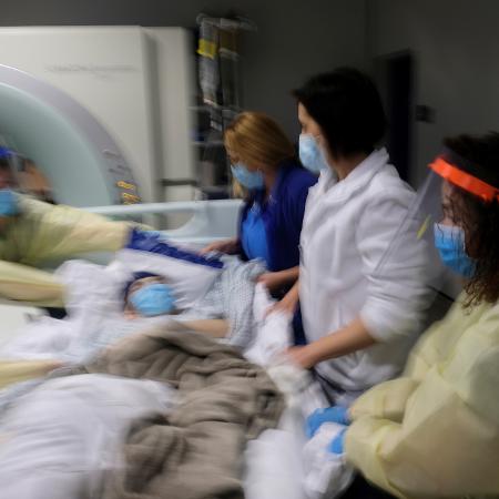 Enfermeiros e radioterapeutas erguem Becs de um aparelho de tomografia computadorizada após uma sessão planejada de radioterapia. 