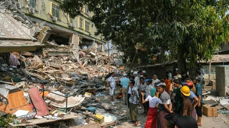 Pessoas observam enquanto equipes de resgate tentam libertar moradores presos sob os escombros do empreendimento destruído Sky Villa Condominium em Mandalay em 29 de março de 2025, um dia após um terremoto atingir o centro de Mianmar Pessoas observam enquanto equipes de resgate tentam libertar moradores presos sob os escombros do empreendimento destruído Sky Villa Condominium em Mandalay em 29 de março de 2025, um dia após um terremoto atingir o centro de Mianmar