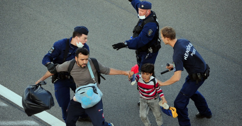 8.set.2015 - Família de refugiados é hostilizada pela polícia em estrada próxima à Röszke, cidade localizada na fronteira entre Hungria e Sérvia
