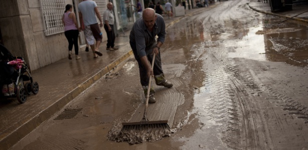 Homem tenta limpar a rua com uma vassoura na cidade de Adra, no sul da Espanha - José Guerrero/AFP