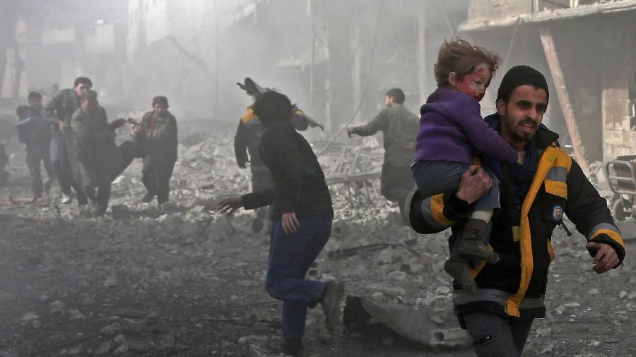 19.fev.2018 - Homem sírio carrega criança ferida em bombardeio na cidade rebelde de Hamouria, em Ghouta Oriental, perto da capital da Síria, Damasco - Abdulmonam Eassa/AFP
