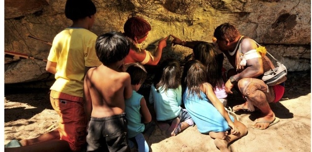 Um índio Waurá ensinando a mitologia em torno do guerreiro Kamukuwaká a crianças da aldeia usando as gravuras da caverna no Xingu antes do local ser vandalizado - Divulgação/People’s Palace Project