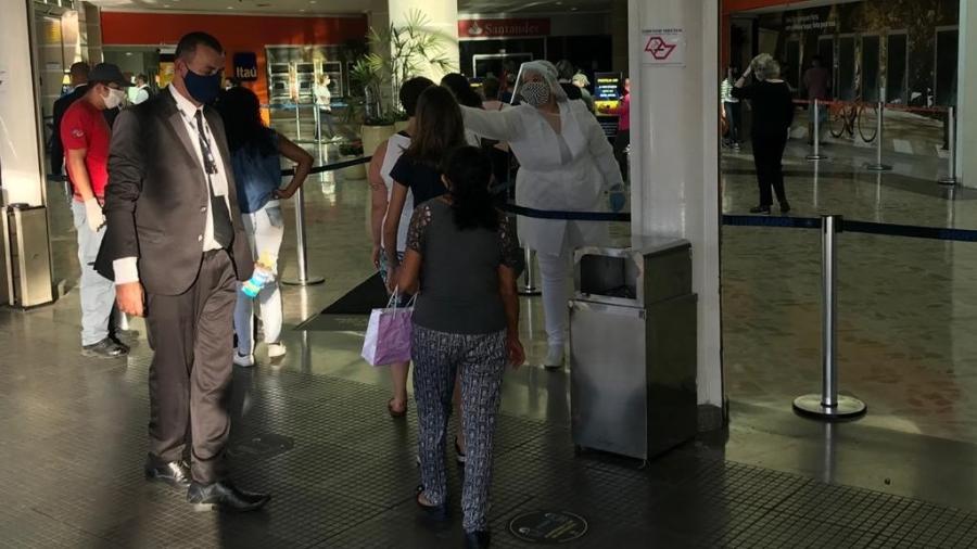 Funcionária mede a temperatura de frequentadores na entrada do Shopping Interlagos, em São Paulo  - Felipe Pereira/UOL