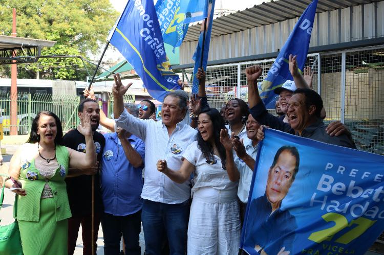 1º.out.2024 - Bebetto Haddad (DC), a vice de branco (ao lado) e correligionários entoam 'grito de guerra' no Mercadão da Penha