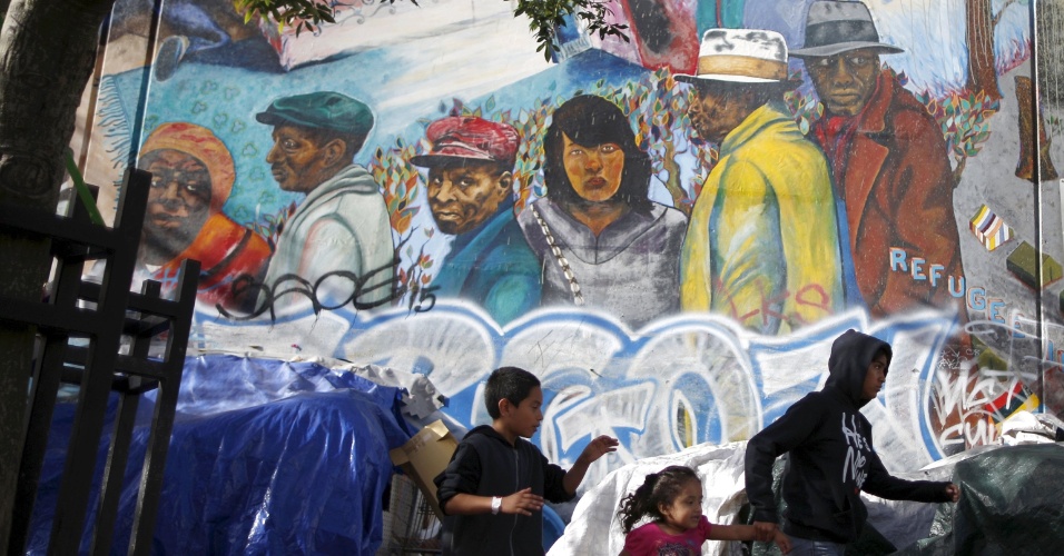 2.out.2015 - Jovens passam por grande mural em Skid Row, no centro de Los Angeles, na Califórnia, EUA