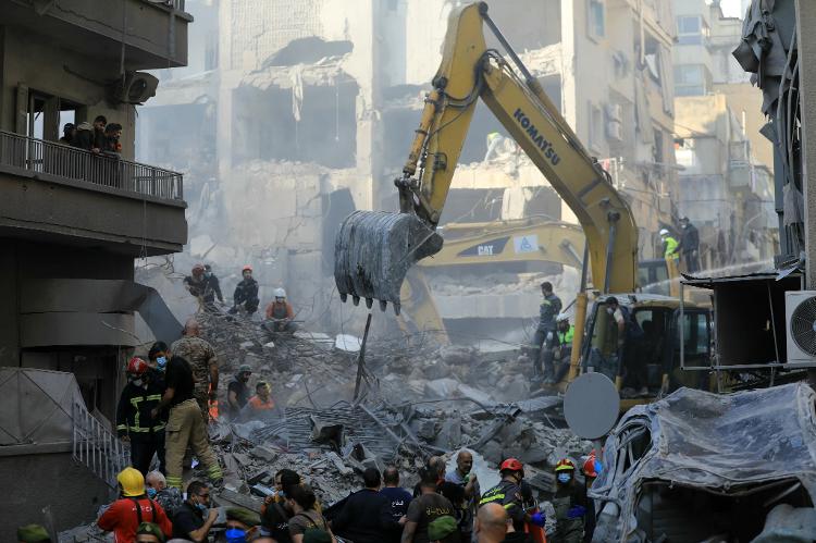 Equipes de resgate usam uma escavadeira para vasculhar os escombros de um prédio destruído, após um ataque aéreo israelense noturno que atingiu o bairro de Basta