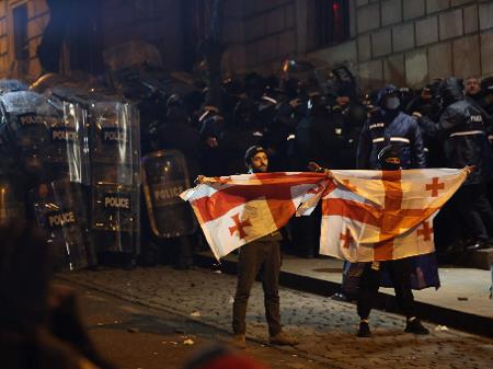 Manifestantes levantam bandeira da Géorgia em Tiblissi, à frente de forças policiais do país; ao menos 44 ficaram feridos por repressão aos protestos na noite de sábado (30) - AFP