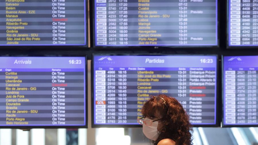 Mulher com máscara de proteção passa por painéis com lista de voos no aeroporto de Viracopos, em Campinas (SP) - Rahel Patrasso