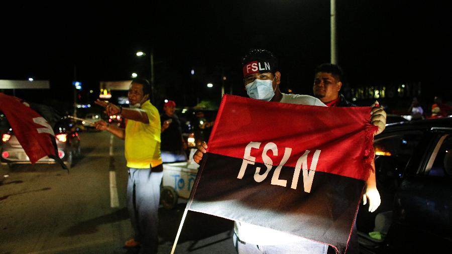 Apoiadores de Daniel Ortega erguem uma bandeira da FSLN enquanto comemoram sua reeleição na Victoria Square, em Manágua - Oswaldo Rivas/AFP