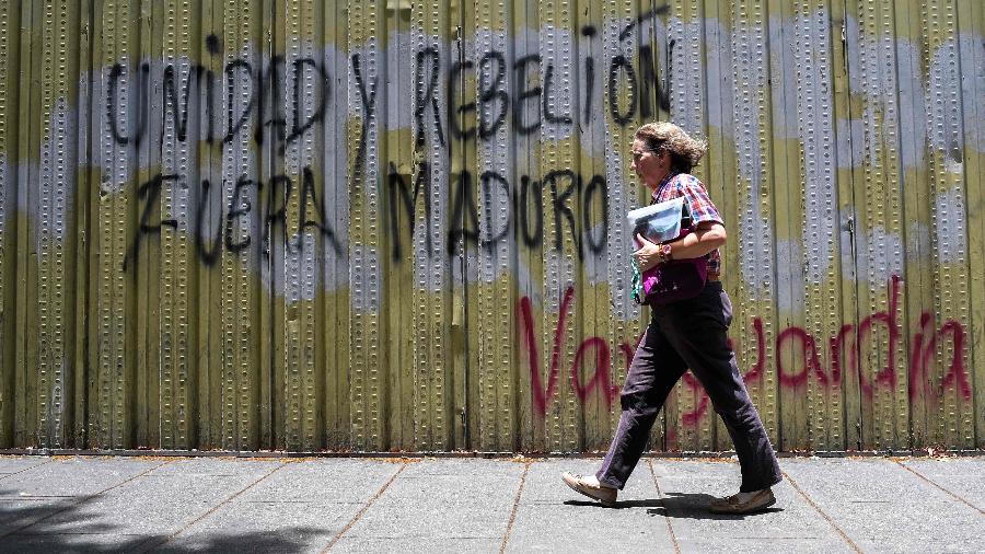 2.mai.2019 - Mulher passa por muro pichado em que está escrito "unidade e rebelião, fora, Maduro", em Caracas, onde pessoas foram mortas durante os protestos - Federico Parra/AFP