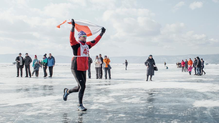 Um corredor da Polônia carrega uma bandeira polonesa enquanto cruza a linha de chegada da maratona na superfície congelada do Lago Baikal, na Rússia - Emile Ducke/The New York Times