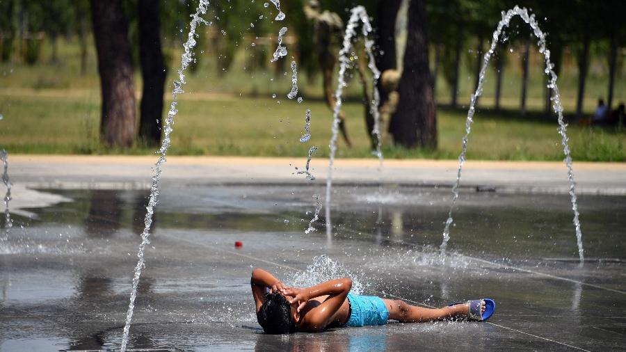27.jun.2019 - Menino deita no chão para aproveitar uma fonte de água em Montpellier, no sul da França  - Pascal Guyot/AFP