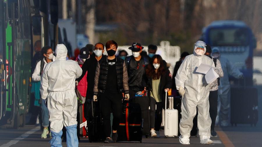 Funcionários com roupa de proteção acompanham passageiros no aeroporto internacional de Pequim - THOMAS PETER