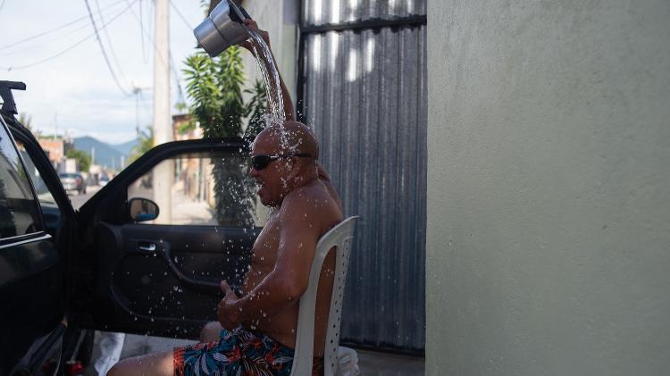 Homem joga balde de água sobre a cabeça para se refrescar em Guaratiba