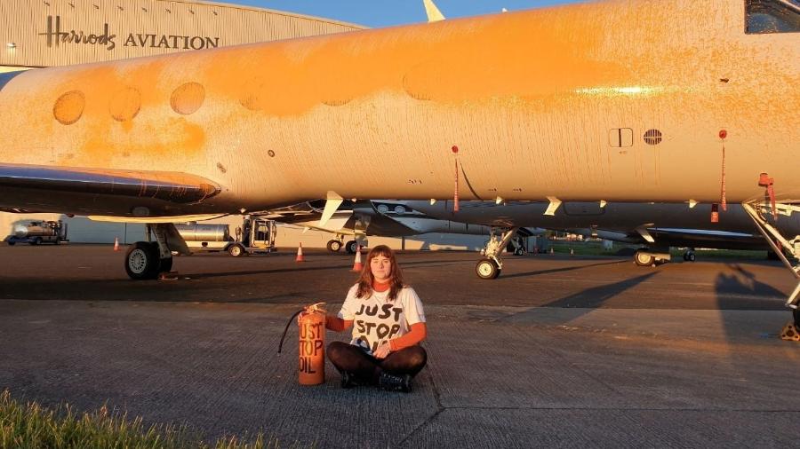 Um manifestante senta-se na frente de uma aeronave enquanto membros do Just Stop Oil pintam aviões em spray no aeroporto de Stansted, Grã-Bretanha, em 20 de junho de 2024