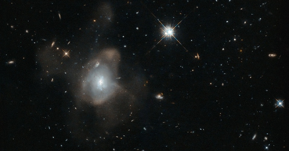 25.nov.2015 - DANÇA NO ESPAÇO - Uma galáxia curiosa, oficialmente conhecida por 2MASX J16270254+4328340, foi fotografada pelo telescópio espacial Hubble fazendo a "dança da fusão galáctica". O que acontece é que a galáxia se fundiu com outra, deixando uma névoa fina feita de milhões de estrelas, que se mexem e criam uma longa cauda. O "tango gravitacional" foi registrado pelo telescópio no momento de conclusão do evento. Essa galáxia está caminhando para sua velhice, com seus dias de formação de estrelas chegando ao fim. À medida que a força da colisão das galáxias diminuir, as estrelas ficarão avermelhadas e começarão a esfriar e escurecer uma por uma