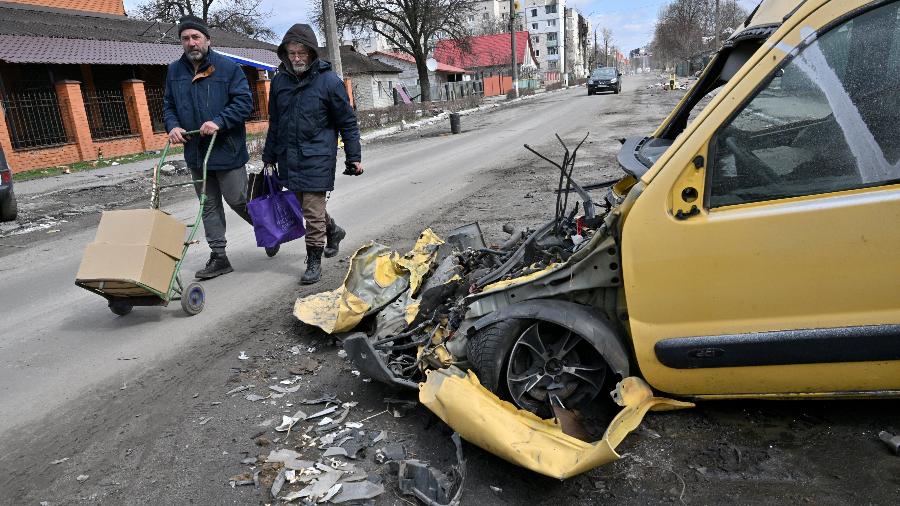 04.abr.2022 - Dois homens passam por um veículo destruído na cidade de Borodianka, a noroeste de Kiev - SERGEI SUPINSKY / AFP
