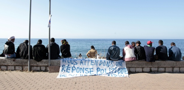 Imigração é tema de tensão entre países há anos; em foto de 2015, migrantes esperam para atravessar a fronteira, na faixa lê-se: "Estamos esperando por uma resposta política" - Jean Christophe Magnenet/AFP