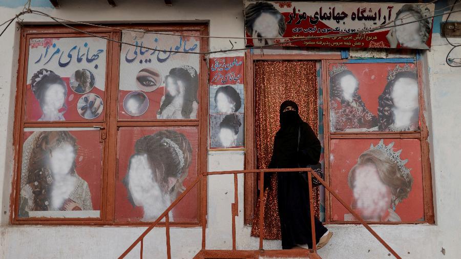 Mulher vestindo um niqab entra em um salão de beleza onde os anúncios de mulheres foram desfigurados por um lojista em Cabul, Afeganistão, 6 de outubro de 2021 - JORGE SILVA/REUTERS