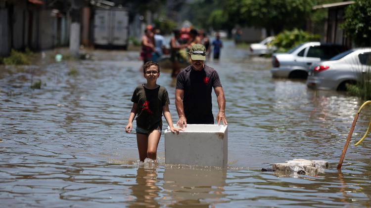Pessoas carregam pertences por ruas alagadas de Duque de Caxias, no Rio de Janeiro, após fortes chuvas que atingiram a região