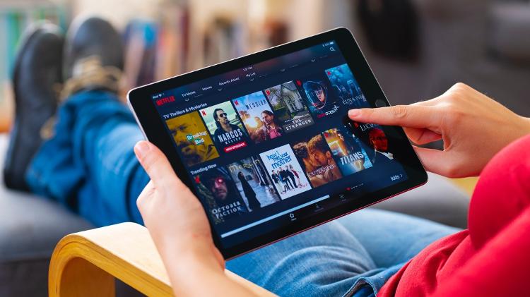 Mulher deitada em sofá com app da Netflix aberto em tablet - Getty Images - Getty Images