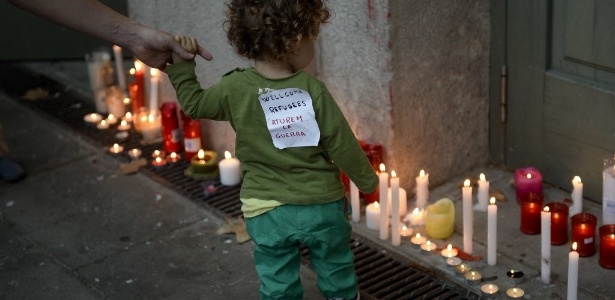 Criança passa por velas acesas em tributo a imigrantes sírios em uma estação de trem em Barcelona, na Espanha. "Bem-vindos, refugiados. Parem a guerra", se lê em mensagem escrita em catalão colada em sua camiseta - Josep Lago/AFP